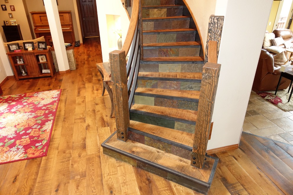 Пример оригинального дизайна: большая изогнутая лестница в стиле рустика с деревянными ступенями, подступенками из сланца и деревянными перилами