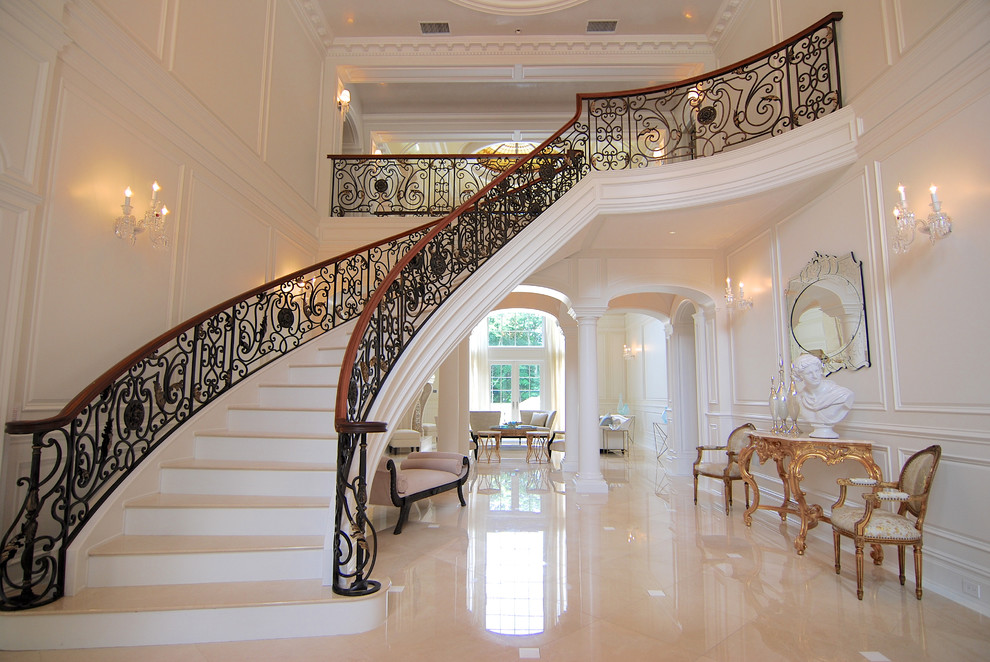 Cette photo montre un grand escalier courbe chic en marbre avec des contremarches en marbre et un garde-corps en métal.