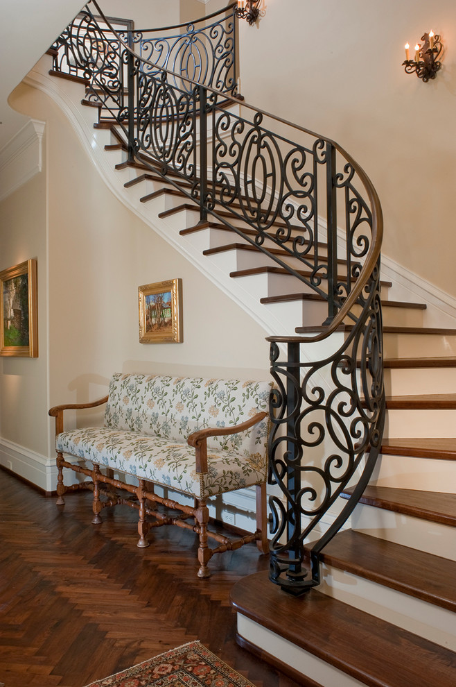 Пример оригинального дизайна: большая изогнутая лестница в средиземноморском стиле с деревянными ступенями и крашенными деревянными подступенками