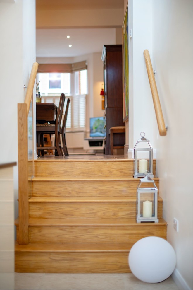 На фото: прямая лестница среднего размера в современном стиле с деревянными ступенями, подступенками из травертина и стеклянными перилами с