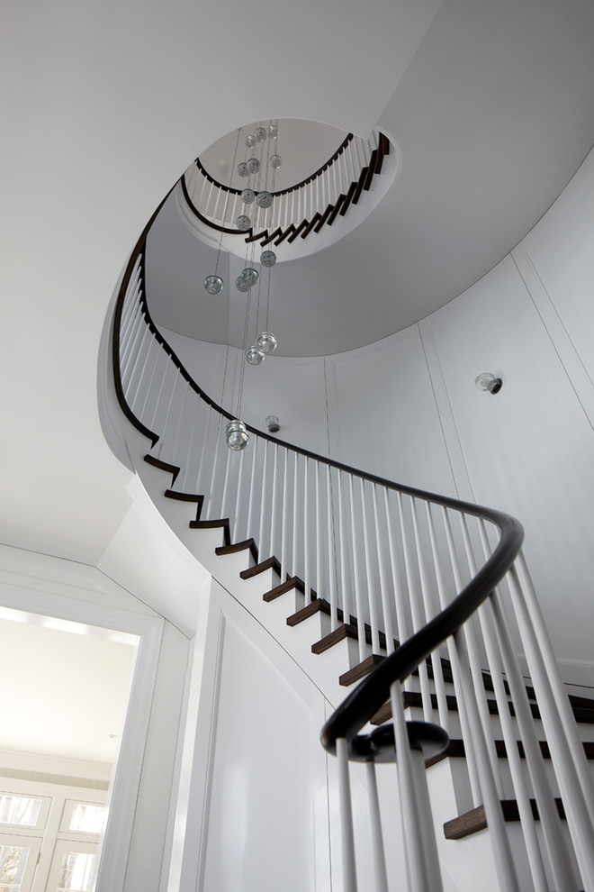 Идея дизайна: большая винтовая лестница в стиле неоклассика (современная классика) с деревянными ступенями, крашенными деревянными подступенками и деревянными перилами