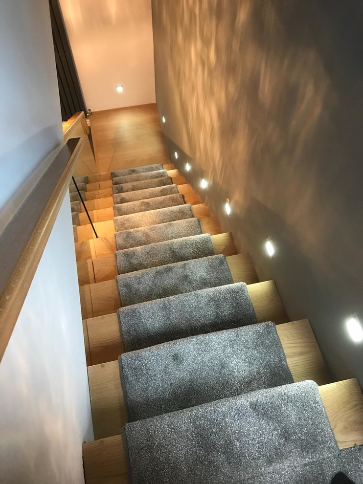 Imagen de escalera recta minimalista de tamaño medio con escalones de madera, contrahuellas de madera y barandilla de vidrio