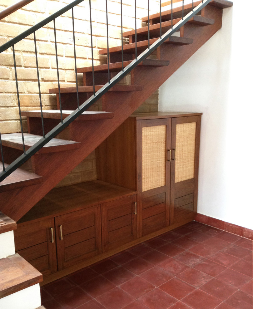 На фото: лестница в восточном стиле с деревянными ступенями и кладовкой или шкафом под ней без подступенок с
