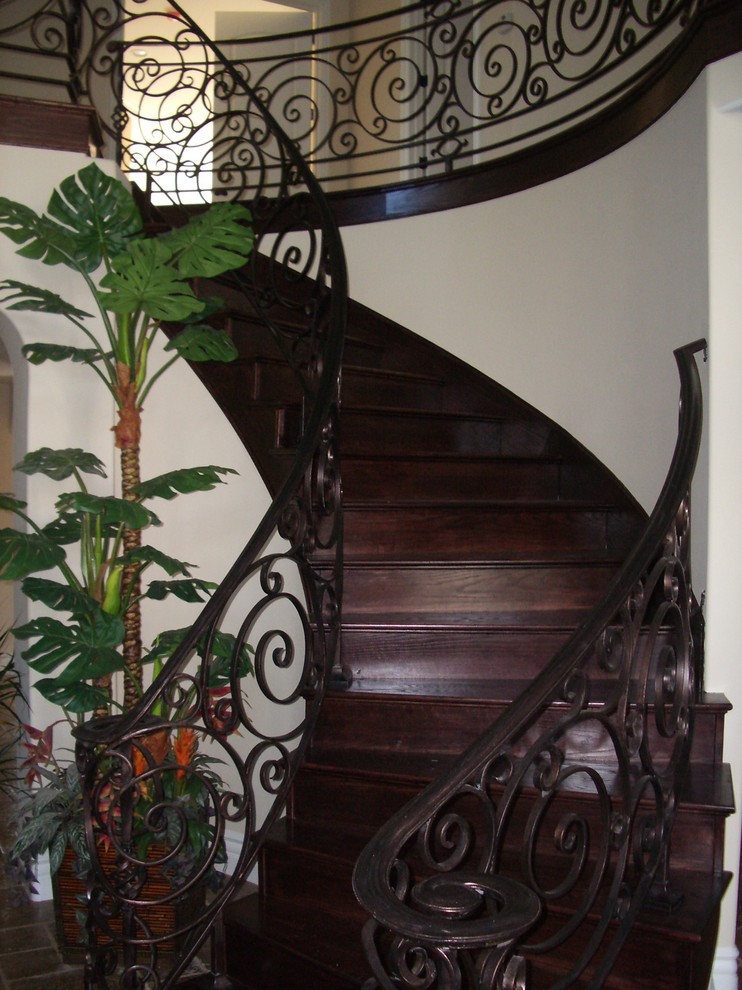 На фото: изогнутая деревянная лестница среднего размера в средиземноморском стиле с деревянными ступенями и металлическими перилами с