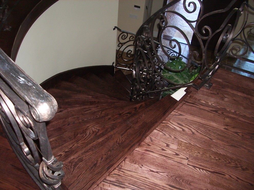 На фото: изогнутая деревянная лестница среднего размера в средиземноморском стиле с деревянными ступенями и металлическими перилами с
