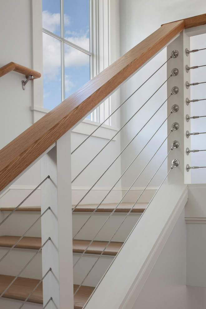 Diseño de escalera actual con escalones de madera, contrahuellas de madera pintada y barandilla de cable