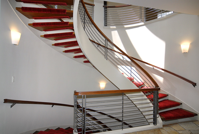 Idée de décoration pour un grand escalier peint courbe design avec des marches en moquette et un garde-corps en matériaux mixtes.