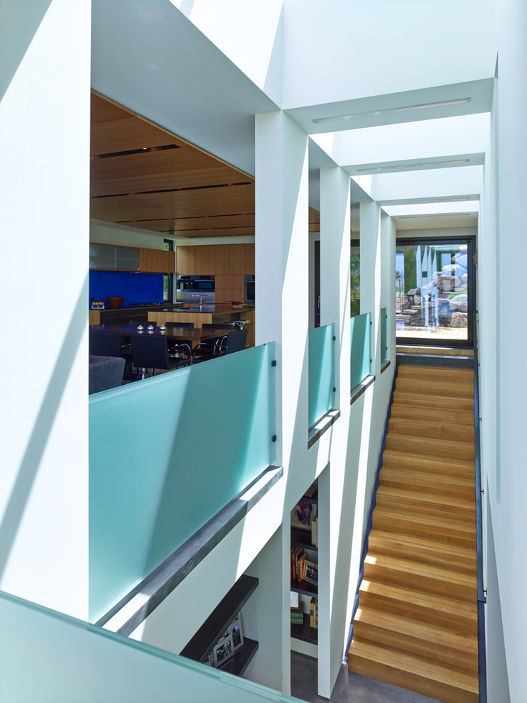 他の地域にある広いコンテンポラリースタイルのおしゃれな直階段 (木の蹴込み板、ガラスフェンス) の写真