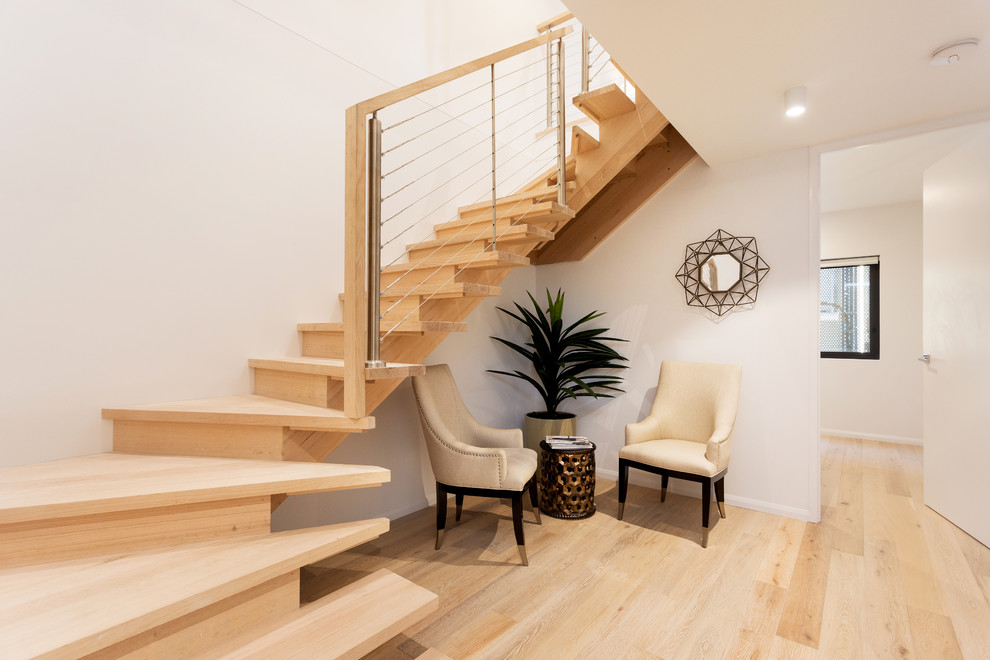 Imagen de escalera en L actual con escalones de madera, contrahuellas de madera y barandilla de cable