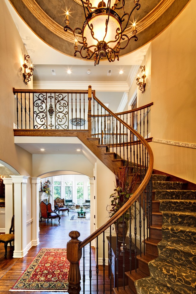 Пример оригинального дизайна: большая изогнутая деревянная лестница в классическом стиле с деревянными ступенями и перилами из смешанных материалов