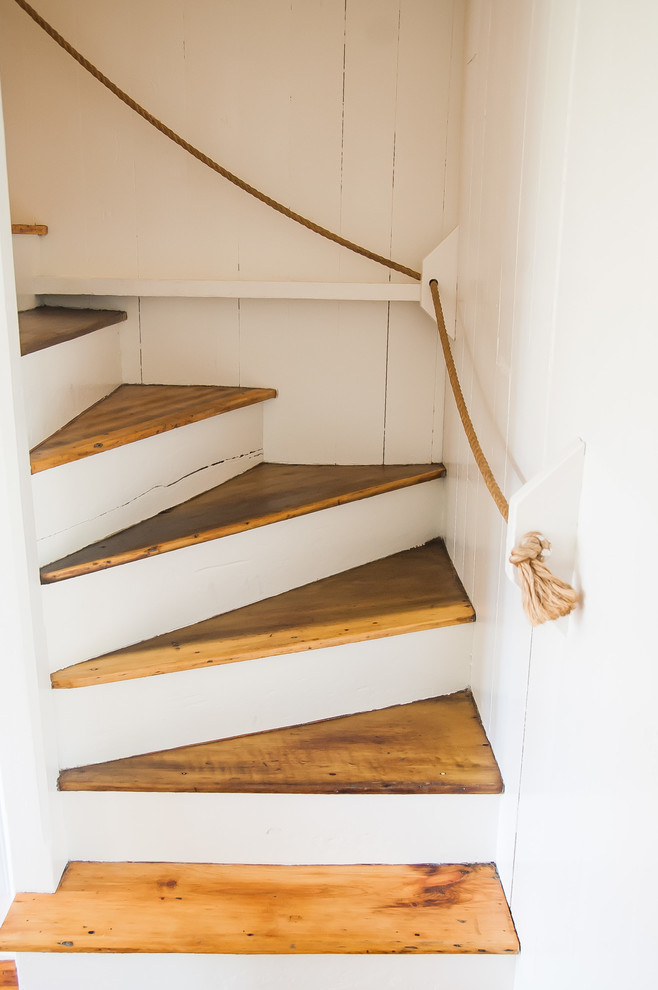 На фото: изогнутая лестница среднего размера в морском стиле с деревянными ступенями и крашенными деревянными подступенками с