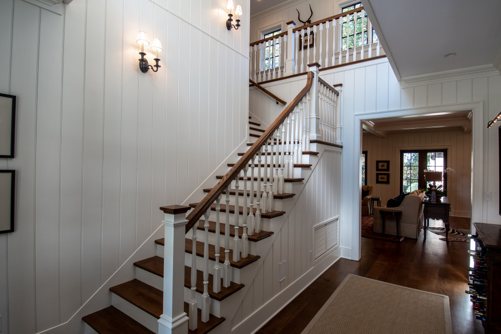 На фото: большая угловая лестница в стиле кантри с деревянными ступенями, крашенными деревянными подступенками и деревянными перилами с
