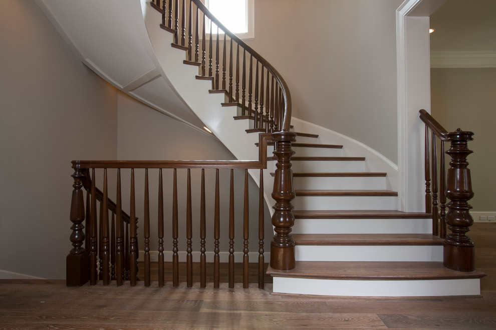Cette image montre un très grand escalier peint courbe traditionnel avec des marches en bois et un garde-corps en bois.