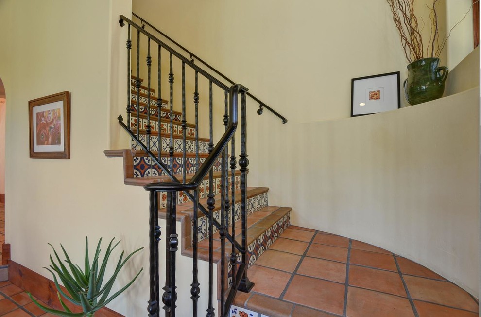 Modelo de escalera mediterránea con escalones de terracota, contrahuellas con baldosas y/o azulejos y barandilla de metal