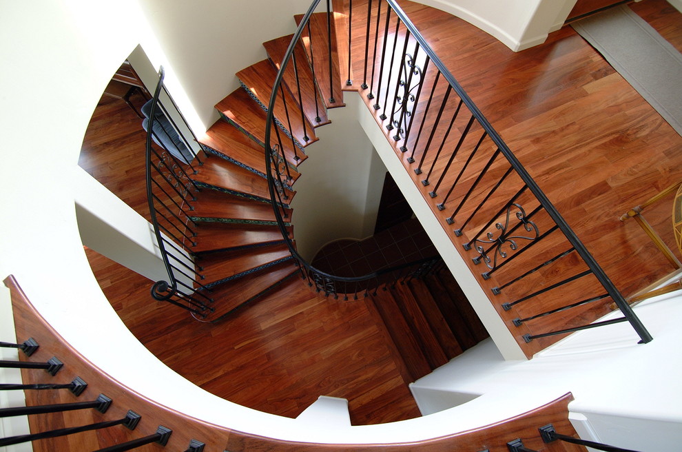 Foto de escalera curva tradicional grande con escalones de madera, contrahuellas con baldosas y/o azulejos y barandilla de metal