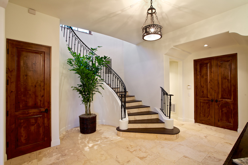Large tuscan wooden curved metal railing staircase photo in San Diego with travertine risers