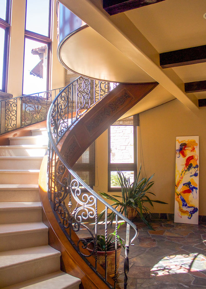 На фото: большая изогнутая лестница в средиземноморском стиле с ступенями из известняка, подступенками из известняка и металлическими перилами с