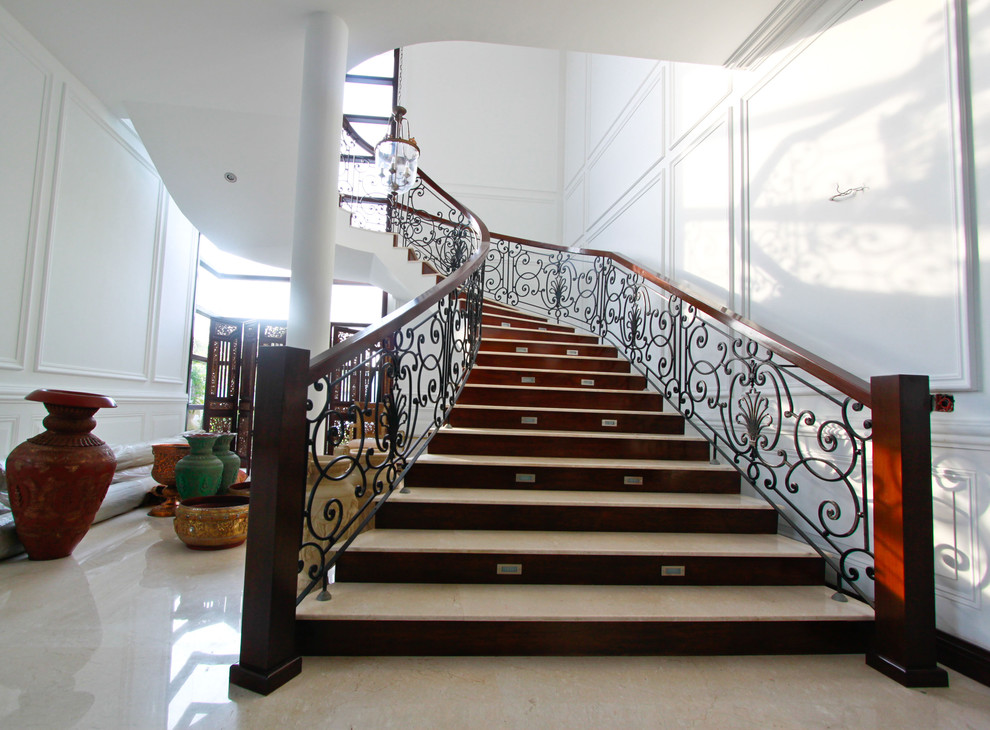Ejemplo de escalera curva mediterránea con escalones de travertino, contrahuellas de madera y barandilla de metal
