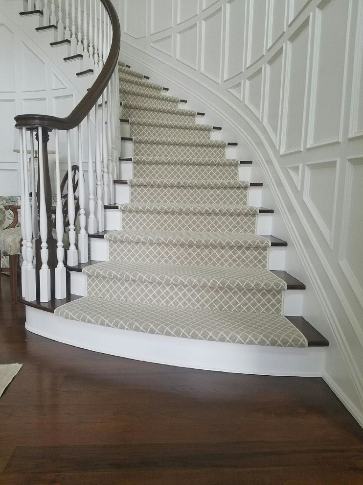 Imagen de escalera curva tradicional grande con escalones de madera, contrahuellas de madera pintada y barandilla de madera