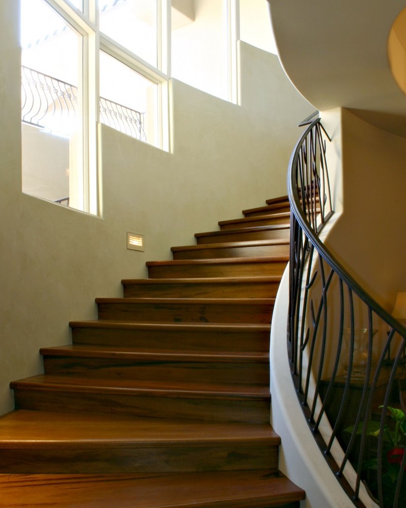 Cette image montre un grand escalier courbe méditerranéen avec des marches en bois et des contremarches en métal.