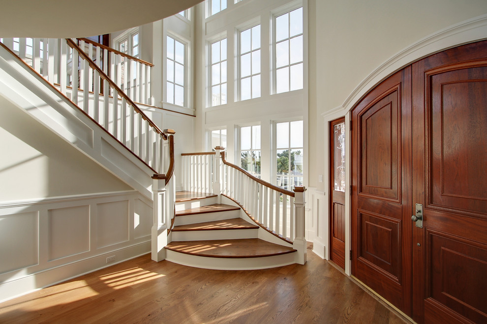 На фото: огромная изогнутая лестница в классическом стиле с деревянными ступенями и крашенными деревянными подступенками