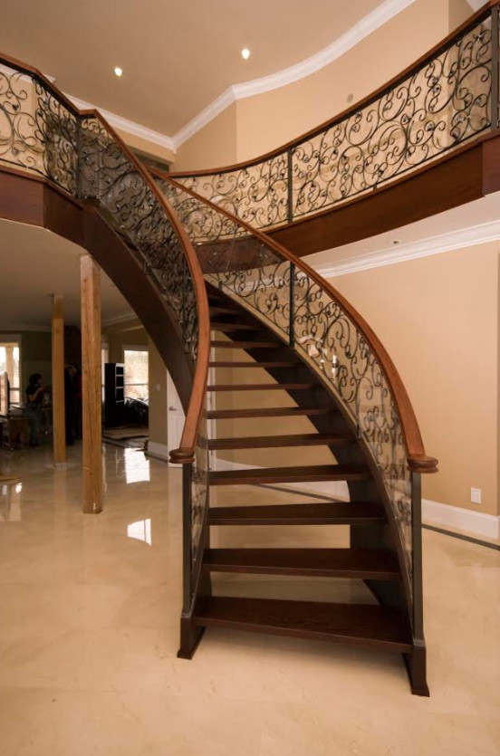 Пример оригинального дизайна: огромная изогнутая лестница в классическом стиле с деревянными ступенями и перилами из смешанных материалов без подступенок
