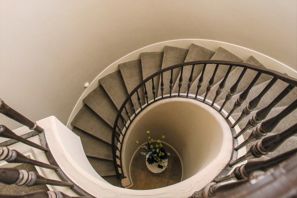 Пример оригинального дизайна: большая изогнутая деревянная лестница в стиле неоклассика (современная классика) с ступенями с ковровым покрытием и металлическими перилами