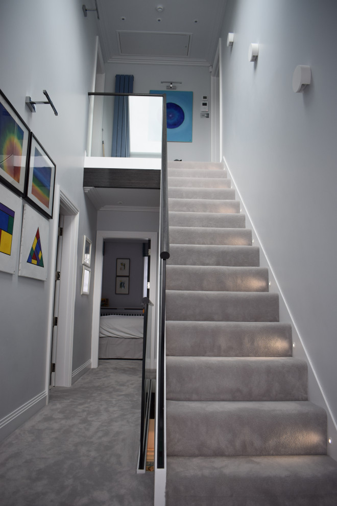 ロンドンにあるラグジュアリーな広いコンテンポラリースタイルのおしゃれな直階段 (カーペット張りの蹴込み板、ガラスフェンス) の写真