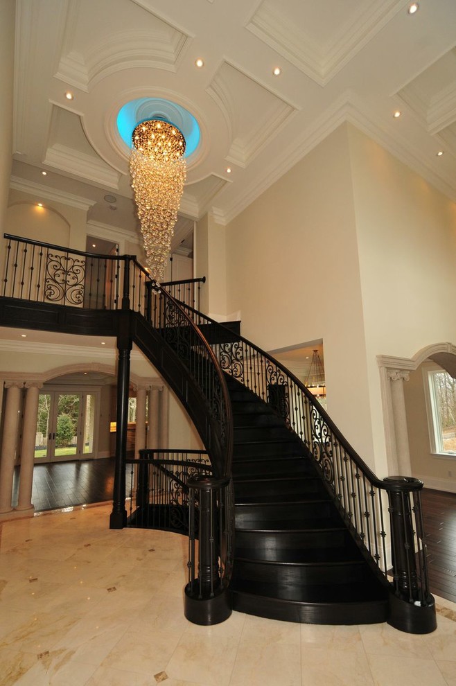 На фото: огромная изогнутая лестница в классическом стиле с крашенными деревянными ступенями и крашенными деревянными подступенками с