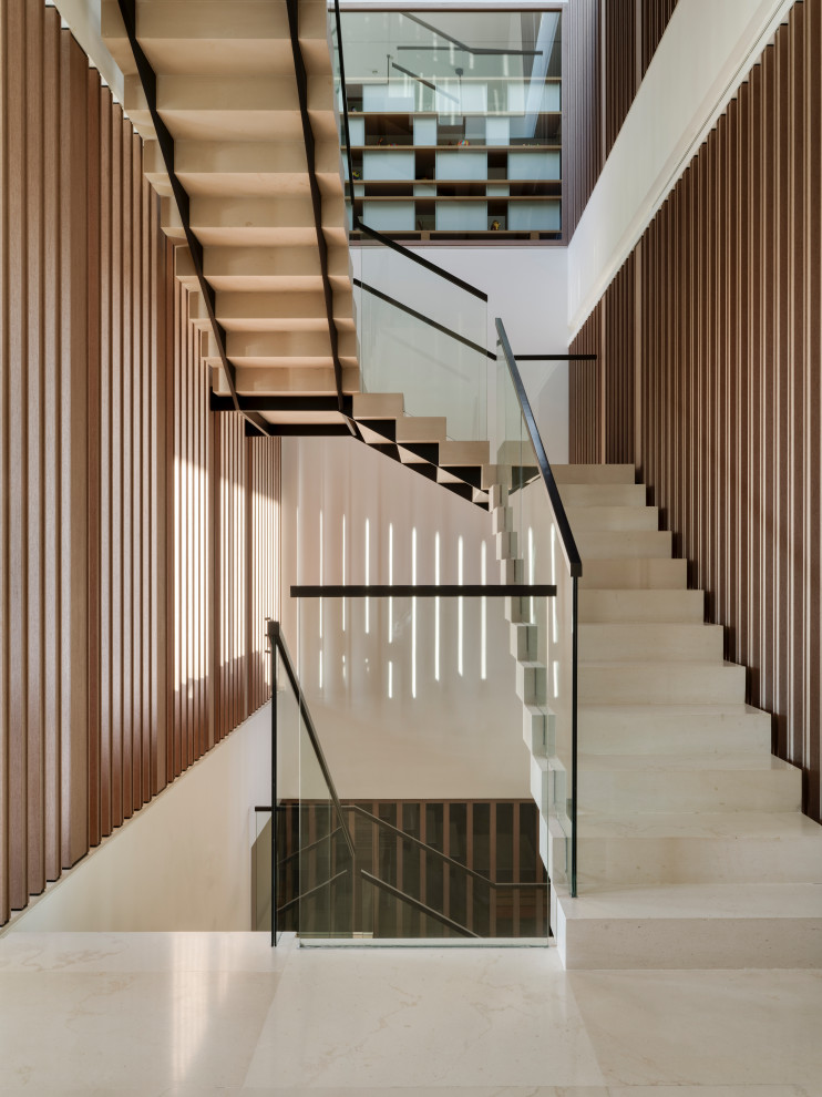 На фото: огромная п-образная лестница в современном стиле с ступенями из известняка, стеклянными перилами и подступенками из известняка