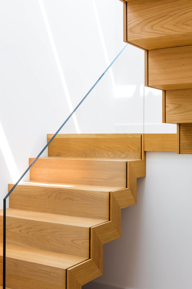 Medium sized wood floating glass railing staircase in Wiltshire with wood risers.