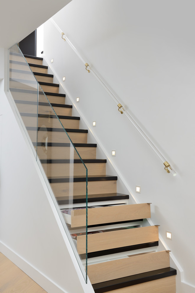 Idée de décoration pour un escalier droit design avec un garde-corps en verre et rangements.