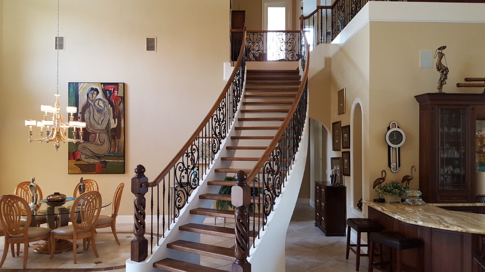 Пример оригинального дизайна: большая изогнутая лестница в средиземноморском стиле с деревянными ступенями и перилами из смешанных материалов без подступенок