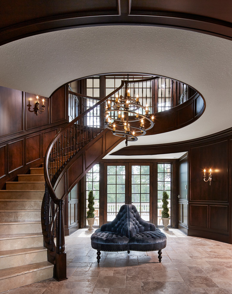 На фото: огромная изогнутая лестница в классическом стиле с деревянными перилами, ступенями из известняка и подступенками из известняка