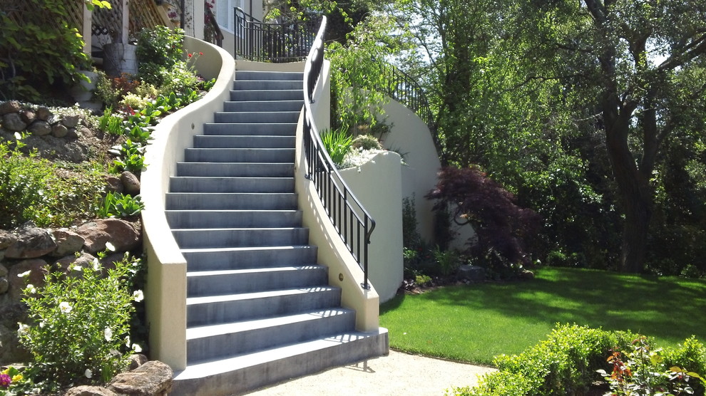 На фото: большая изогнутая бетонная лестница в средиземноморском стиле с бетонными ступенями и металлическими перилами с