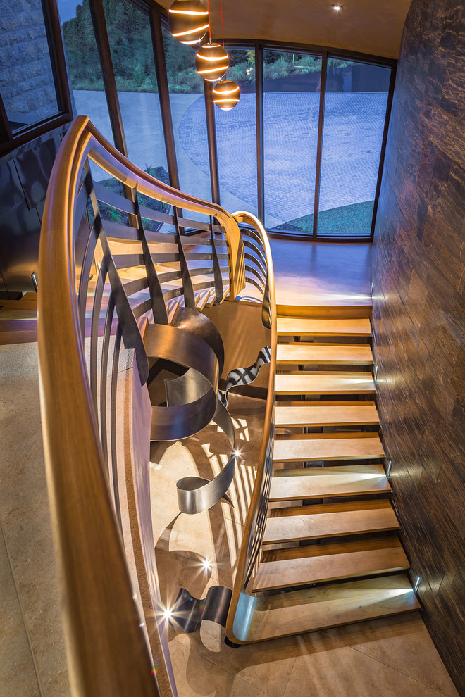 Источник вдохновения для домашнего уюта: огромная изогнутая металлическая лестница в стиле модернизм с деревянными ступенями