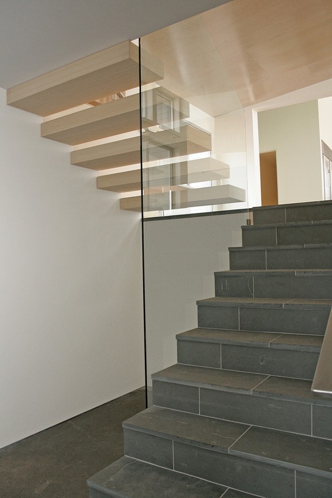 Cette photo montre un escalier carrelé moderne avec un garde-corps en métal et des contremarches carrelées.