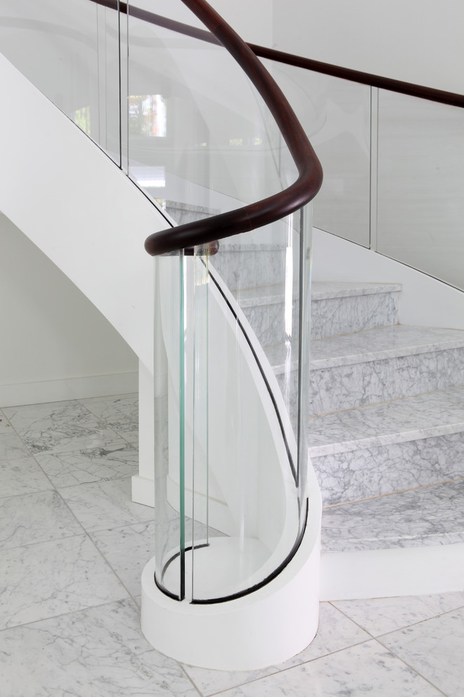 Example of a huge trendy curved glass railing staircase design in Other
