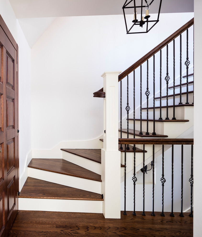 Diseño de escalera tradicional con escalones de madera, contrahuellas de madera pintada y barandilla de metal