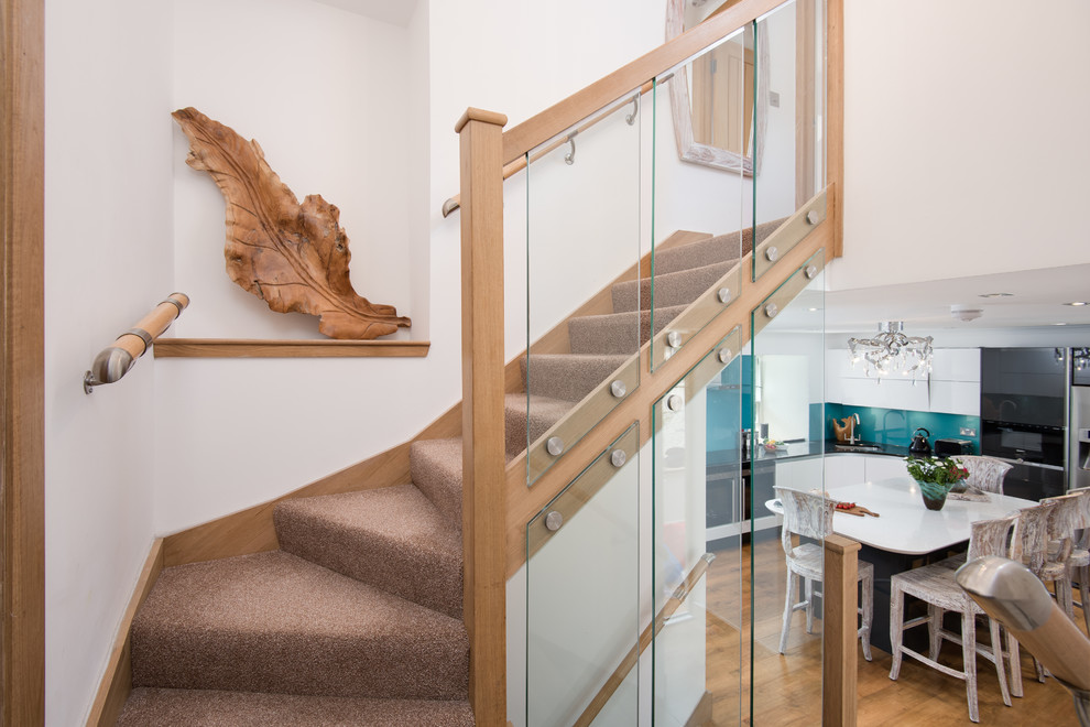 На фото: изогнутая лестница среднего размера в стиле кантри с ступенями с ковровым покрытием, стеклянными подступенками и деревянными перилами с