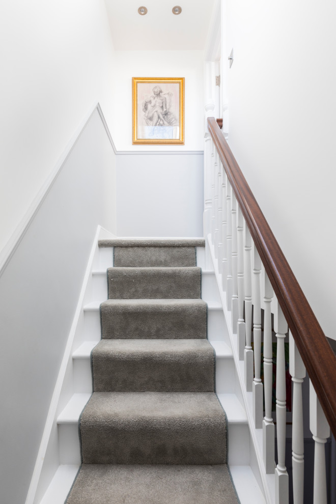 На фото: прямая лестница с ступенями с ковровым покрытием, ковровыми подступенками и деревянными перилами с