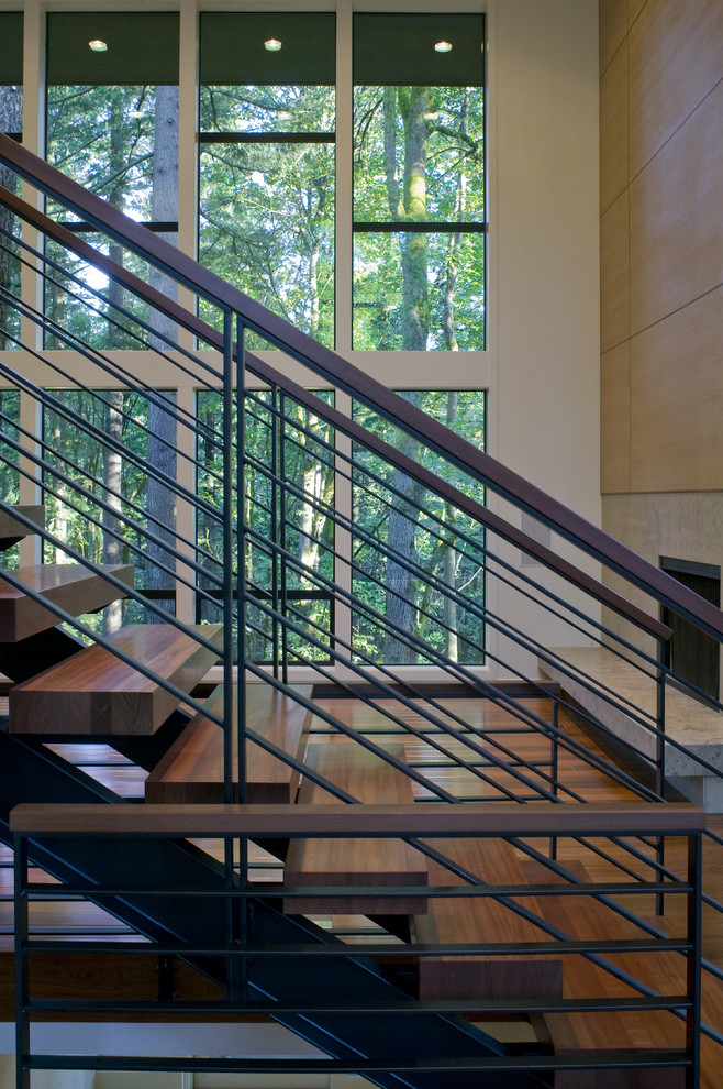 Cette image montre un grand escalier courbe design avec des marches en bois, des contremarches en métal et un garde-corps en bois.