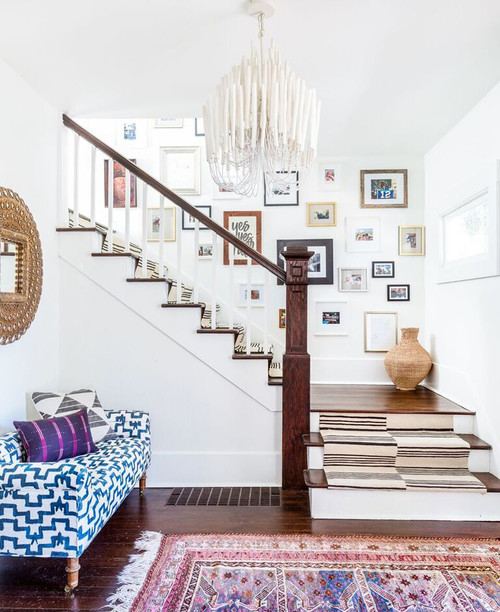 White stairway with eclectic gallery wall and beige striped running on dark wood floors