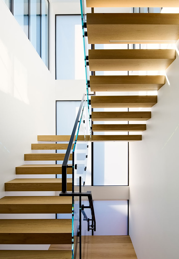 Réalisation d'un petit escalier sans contremarche flottant minimaliste avec des marches en bois et un garde-corps en verre.