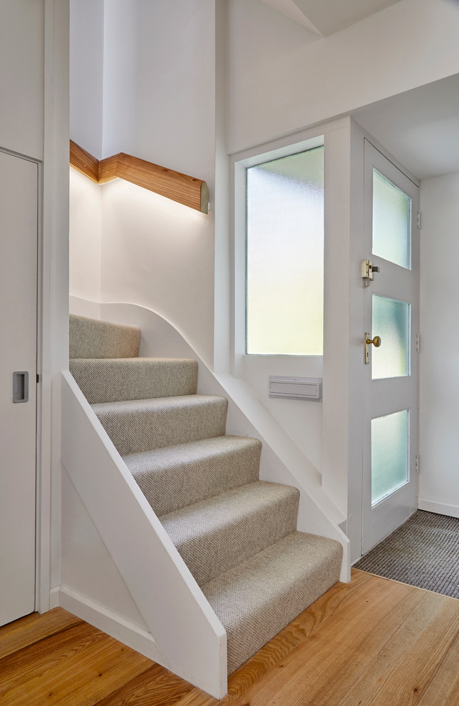 Пример оригинального дизайна: изогнутая лестница в стиле ретро с ступенями с ковровым покрытием, ковровыми подступенками и деревянными перилами