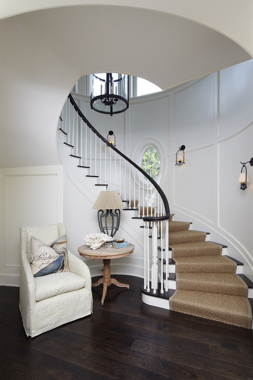 White staircase with dark wood floors and millwork with hanging lantern sconces and small round window on the staircase wall