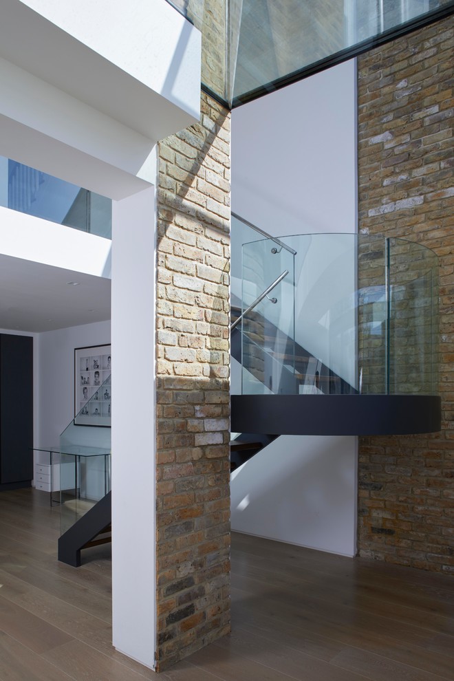 Idée de décoration pour un grand escalier courbe design avec des marches en bois, des contremarches en métal et un garde-corps en verre.