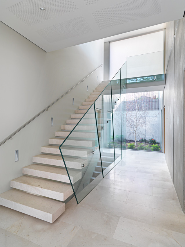 Imagen de escalera suspendida contemporánea de tamaño medio con escalones de piedra caliza, contrahuellas de piedra caliza y barandilla de vidrio