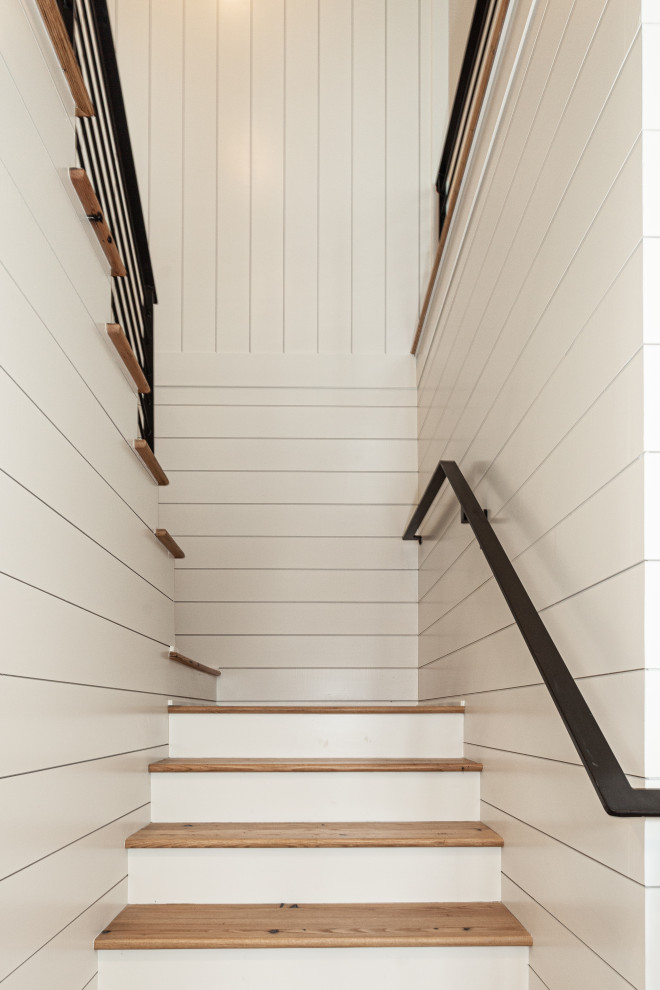 Photo of a large coastal wood u-shaped metal railing staircase in Charleston with painted wood risers and tongue and groove walls.