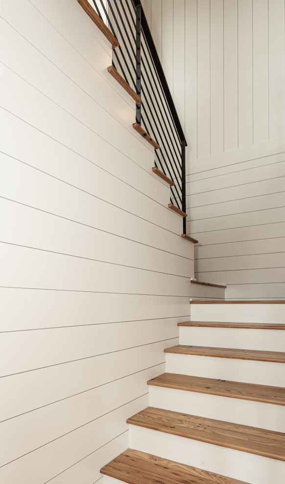 This is an example of a large coastal wood u-shaped metal railing staircase in Charleston with painted wood risers and tongue and groove walls.